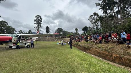 MAF plane at the Kompiam airstrip with a huge crowd of bystanders lined up around the airstrip