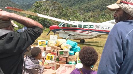 People watch an MAF plane taxi away as they stand by their goods received