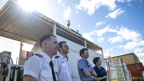 Student pilots andn instructor standing on tarmac watching plane fly by