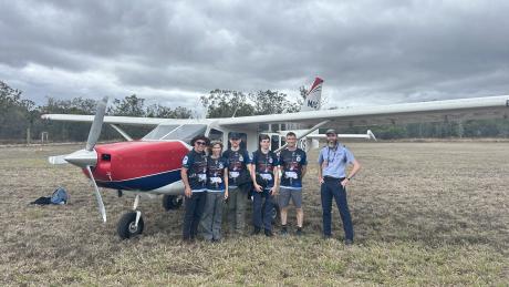 Pilot and passengers standing in front of plane on grass airstrip