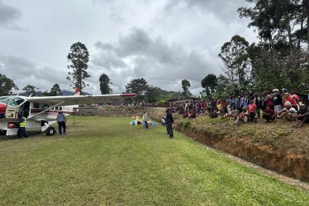 MAF plane at the Kompiam airstrip with a huge crowd of bystanders lined up around the airstrip