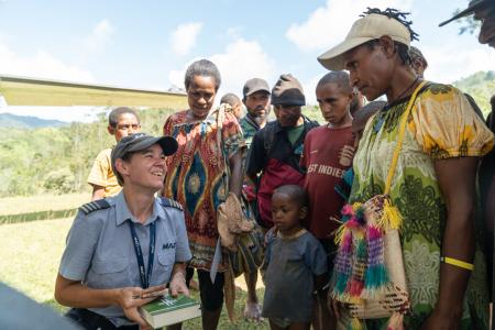 Pilot Bridget Ingham kneeling next to the plane surrounded by a group of people who are all interested to purchase Bibles