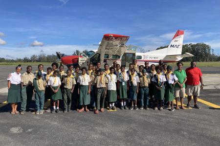 Balimo Pathfinders group standing in front of MAF plane, awaiting flights home to Balimo.