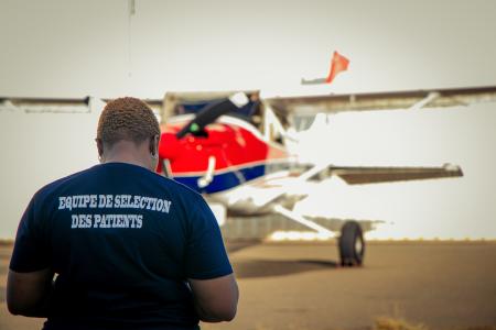 Mercy Ships patient selection staff member stands in front of MAF plane