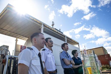 Student pilots andn instructor standing on tarmac watching plane fly by