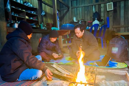 Men huddle around a smartphone by a fire in a hut