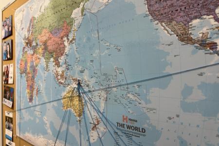 Large world map with strings and pins marking locations.