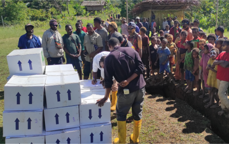 Boxes with medical supplies stacked up after delivering at a remote airstrip, a lot of bystanders watching