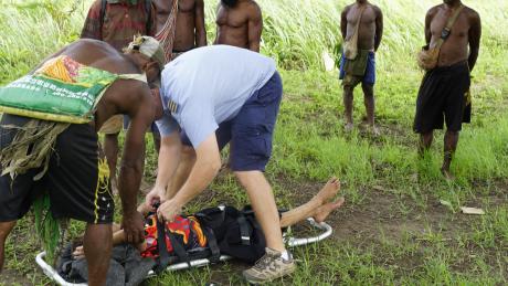 MAF Pilot Tim Neufeld loading a medevac patient onto a stretcher with villager onlookers.
