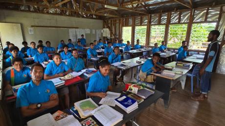 Students in classroom at Mougulu Secondary School sitting on new chairs with teacher Maika Yabua