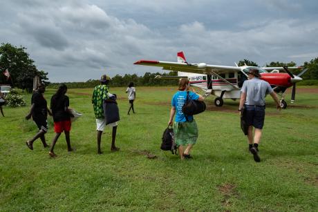 Students, teacher and pilot walking to aircraft on grass airstrip