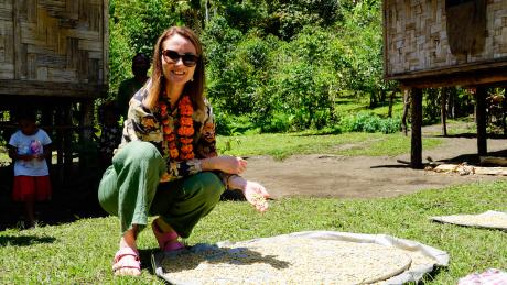 A woman inspects coffee beans drying in the sun in a village setting