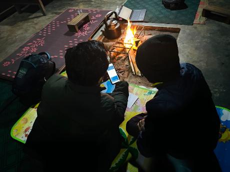 Two men view a smartphone by a fire in a hut