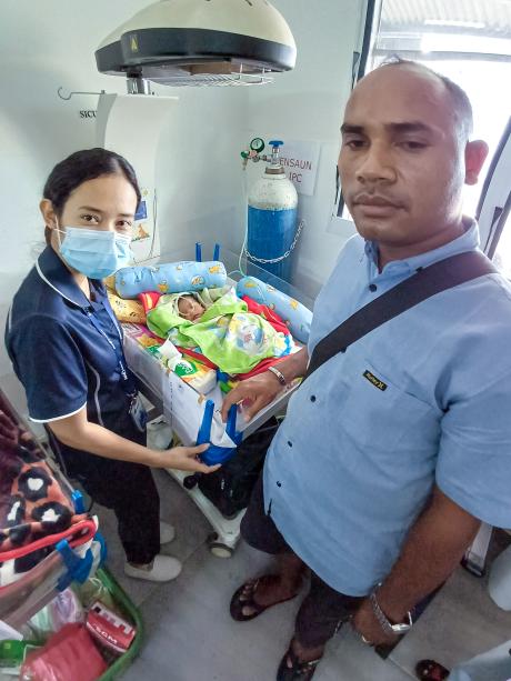 A man and a woman stand next to a baby inside the incubator.